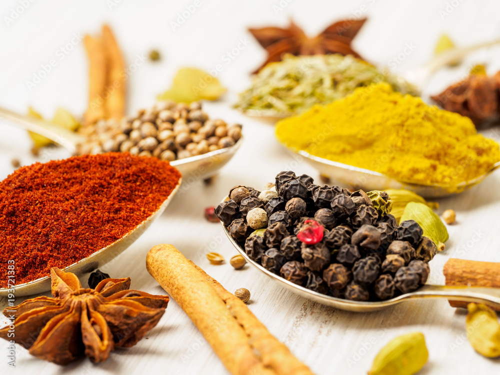 Mix of Indian spices in spoons on white wooden table, side view, selective focus, macro. Seasonings black pepper and paprika, close up Mix of Indian spices in spoons on white wooden table, side view, selective focus, macro. Seasonings black pepper and paprika, close up
