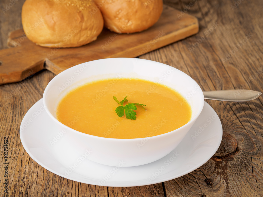white bowl of pumpkin soup, garnished with parsley on wooden background, side view. white bowl of pumpkin soup, garnished with parsley on wooden background, side view.