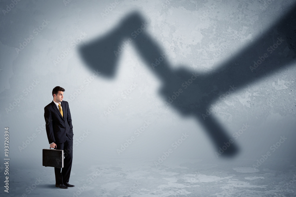 Fototapeta premium Businessman afraid of a huge shadow hand holding an axe concept
