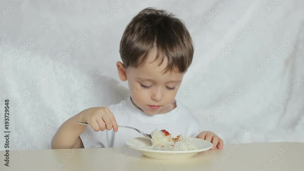 The child boy with pleasure eat soup from dishes with a spoon, close-up. Motion camera slider. A boy eats sitting at a table on a white background. The child boy with pleasure eat soup from dishes with a spoon, close-up. Motion camera slider. A boy eats sitting at a table on a white background.