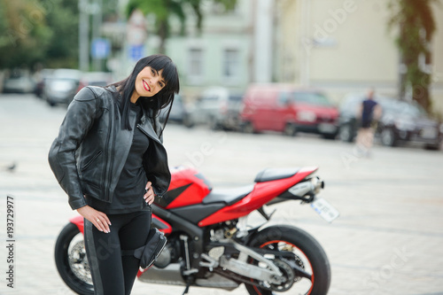 A biker girl in a leather jacket on a motorcycle posing in the city
