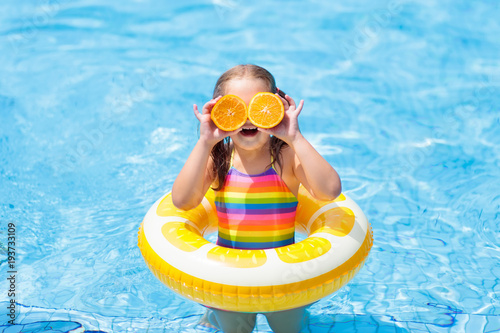 Child in swimming pool. Kid eating orange.