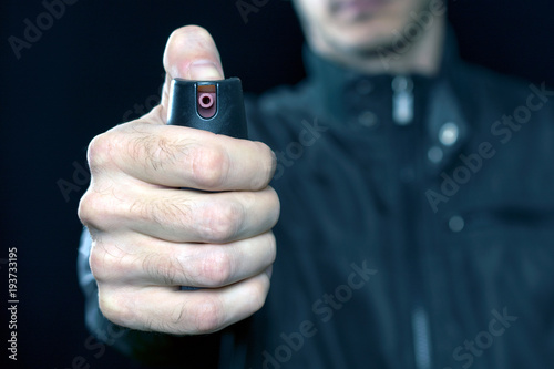 pepper gas in the hand of a young man in a black jacket CS spray self-defense Tear gas concept, close up, selective focus , blurred dark background