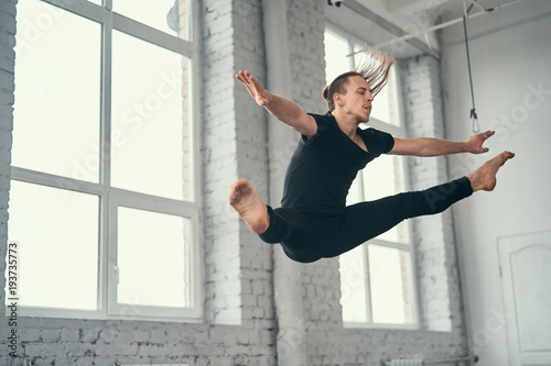 Fototapeta Naklejka Na Ścianę i Meble -  The young attractive modern ballet dancer in black jacket jumping over urban background.