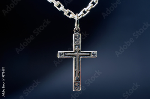 christian cross on a silver chain, faith, spirituality and religion concept. selective focus, dark blurred background