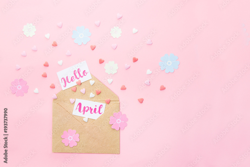 Multicolor sweets sugar candy hearts, handcraft paper flowers and cards with Hello April lettering fly out of craft paper envelope on pink background . Spring concept. Space for text. Horizontal.
