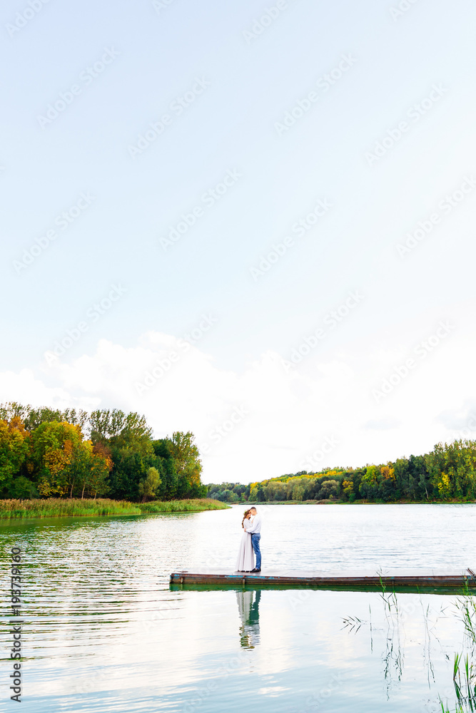 Fototapeta premium The boyfriend hugs his girlfriend standing on the pier on the ba