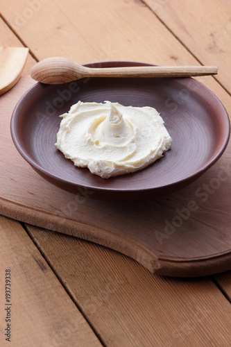 Sour cream on a clay plate on a wooden table, cream on a plate, milk dessert with a wooden spoon, vegan, simple food, retro style milk pattern, rustic style, dairy product, copy space