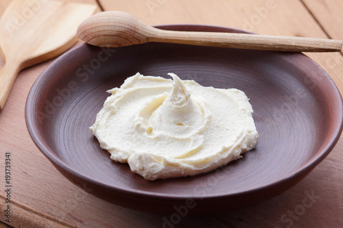 Sour cream on a clay plate on a wooden table, cream on a plate, milk dessert with a wooden spoon, vegan, simple food, retro style milk pattern, rustic style, dairy product, copy space