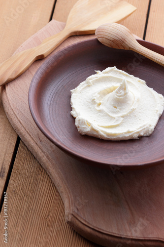 Sour cream on a clay plate on a wooden table, cream on a plate, milk dessert with a wooden spoon, vegan, simple food, retro style milk pattern, rustic style, dairy product, copy space