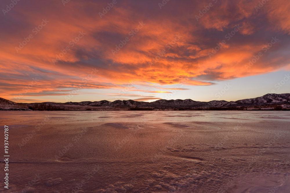 Fiery Clouds - bright and colorful winter sunset clouds rolling over a frozen mountain lake.