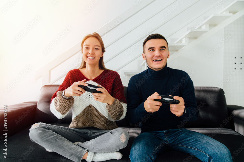 Pretty girl and a guy playing video games online, sitting on couch together, dressed in warm casual clothes. At home. Pretty girl and a guy playing video games online, sitting on couch together, dressed in warm casual clothes. At home.