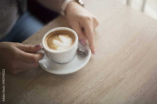 Woman's hands holding cup of coffee on the brown wooden table