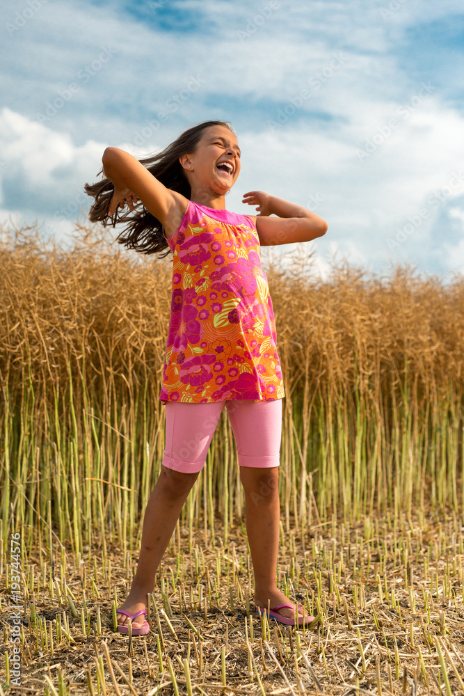Happy little girl in a field of ripe rapeseed - vertical orientation