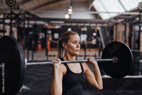 Young woman lifting barbells over her head in a gym