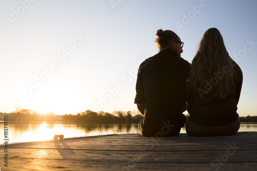 Man and women sit closely together on a dock on a lake