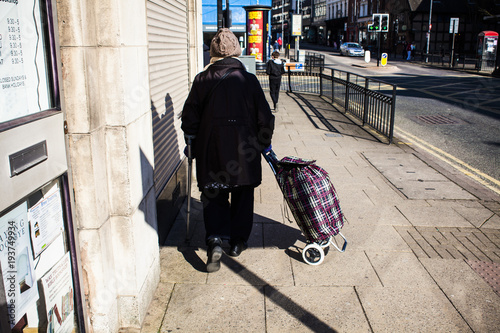 Bild auf Leinwand Old woman walking with trolley, mature female travel in the city