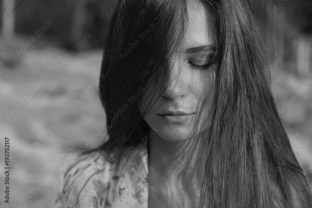 Black and white close up portrait of Caucasian lady meditating closing eyes with sunset rays on face. Portrait of beautiful European female model posing outdoors, standing against nature background. Black and white close up portrait of Caucasian lady meditating closing eyes with sunset rays on face. Portrait of beautiful European female model posing outdoors, standing against nature background.