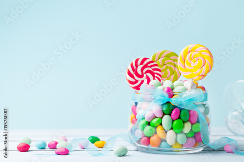 Sweet colorful candy in jar decorated with bow ribbon against blue background. Gifts for Birthday party.