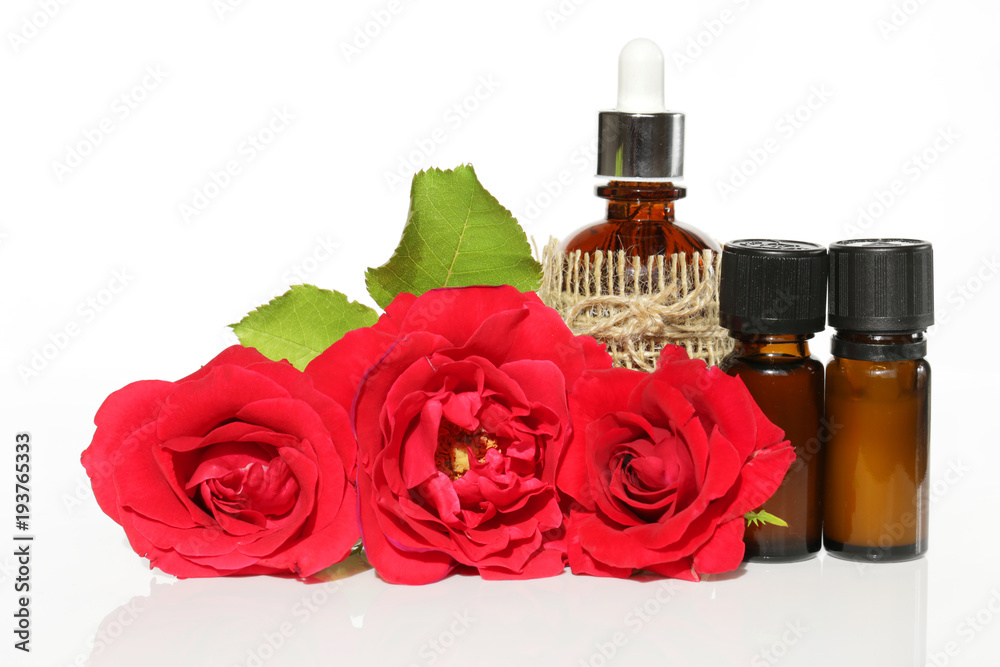 oil roses set. rose essential oil in brown glass bottles and red roses on a white background. Pure Organic Rose Oil oil roses set. rose essential oil in brown glass bottles and red roses on a white background. Pure Organic Rose Oil