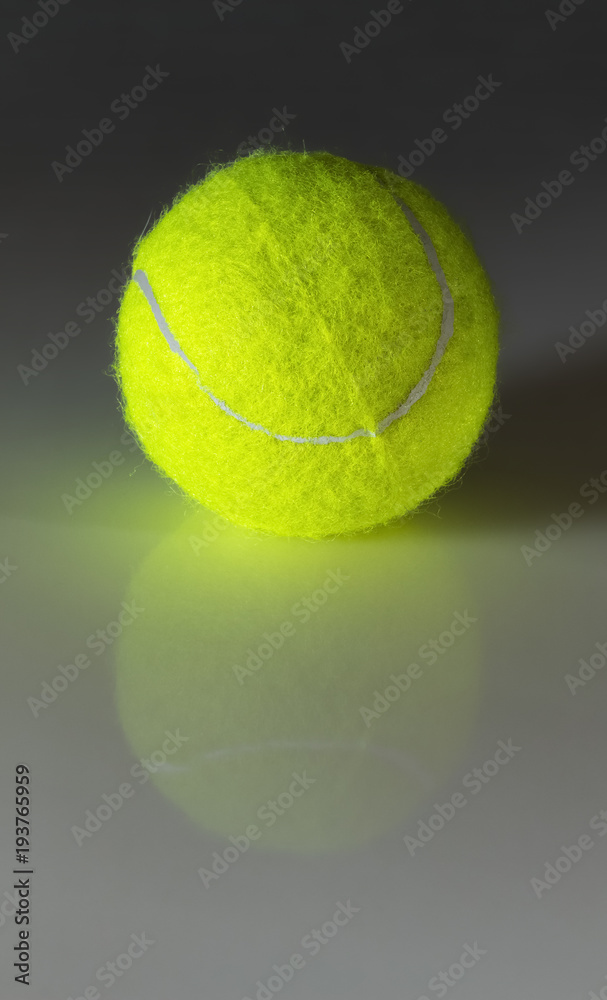 A bright green tennis ball on a smooth white reflection surface close-up.