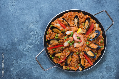 Above view of spanish paella with seafood in a frying pan, view from above on a blue stone background, copyspace