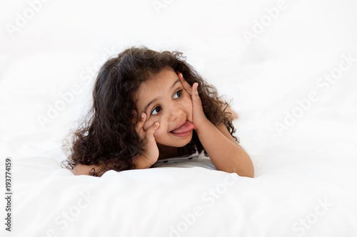 Funny little girl lying on stomach on bed making funny face photo