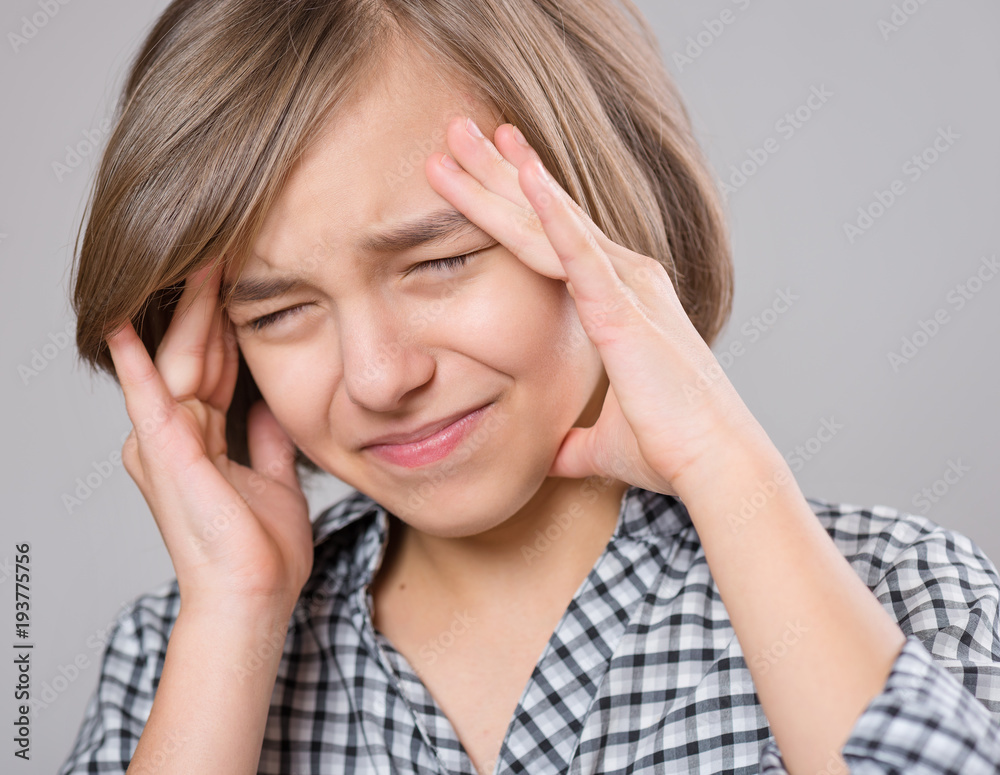 Stress and headache - teen girl having migraine pain. Cute child suffering from a headache. Unhappy caucasian teenager touching her head, on gray background. Stress and headache - teen girl having migraine pain. Cute child suffering from a headache. Unhappy caucasian teenager touching her head, on gray background.