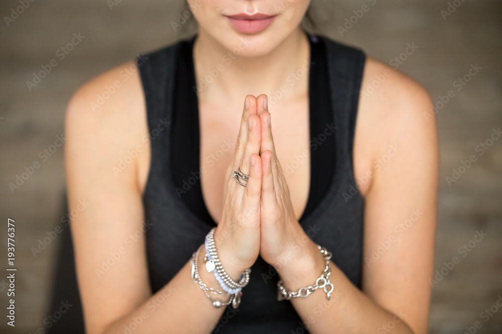 Namaste gesture close up photo, young smiling attractive woman practicing yoga, working out, wearing wrist bracelets and rings, indoor, yoga studio