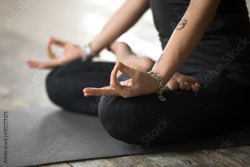 Young sporty woman practicing yoga, doing Padmasana exercise, Lotus pose with mudra gesture, working out, wearing sportswear, black pants and top, indoor close up view, yoga studio