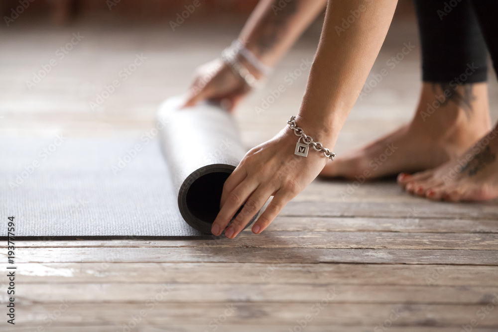Obraz premium Hands of an attractive young woman folding black yoga or fitness mat after working out at home in living room or in yoga studio. Healthy lifestyle, keep fit, weight loss concepts. Close up view photo