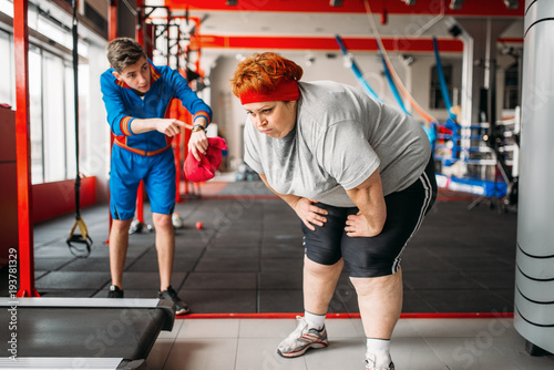 Slika na platnu Instructor forces fat woman to exercise in gym
