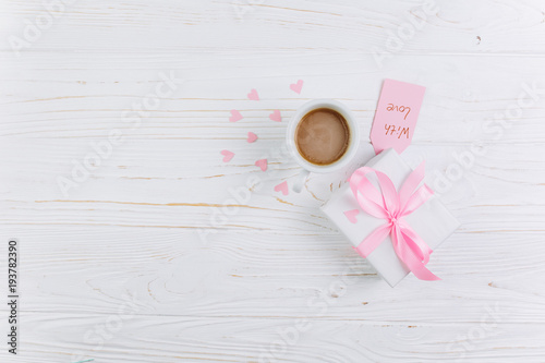 Gift, cup of coffee and paper hearts on a white wooden background, copy space and flat lay. Valentines Day and Mother's Day concept.