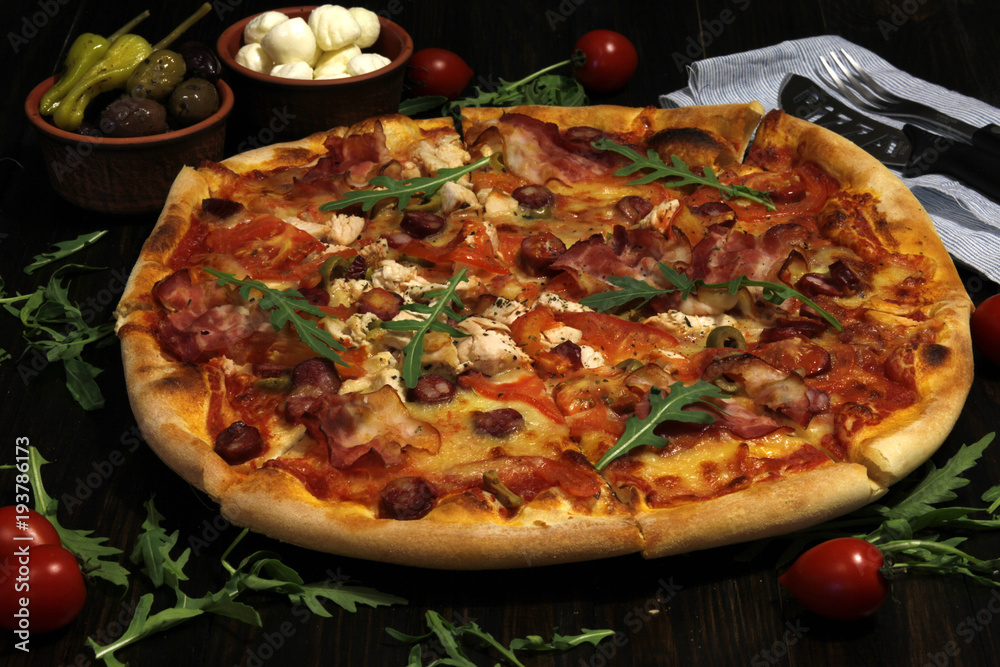Pizza with bacon, sausages, ham, tomato and olives. Sprinkle with arugula and served with tomato and cheese. Pizza Restaurant. Snack, dinner