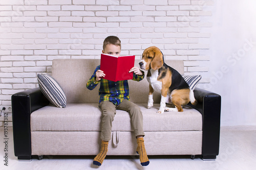 funny boy reading a book with a dog on the couch
