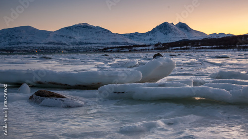 Sunset above the big ice floe in the ocean and mountains with snow on the horizon