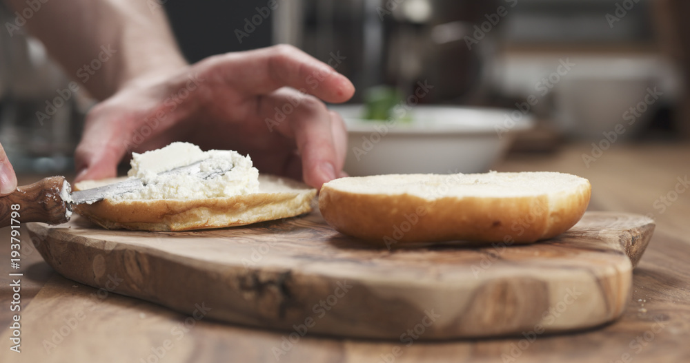 man hands spreading cream cheese on bagel on wood board