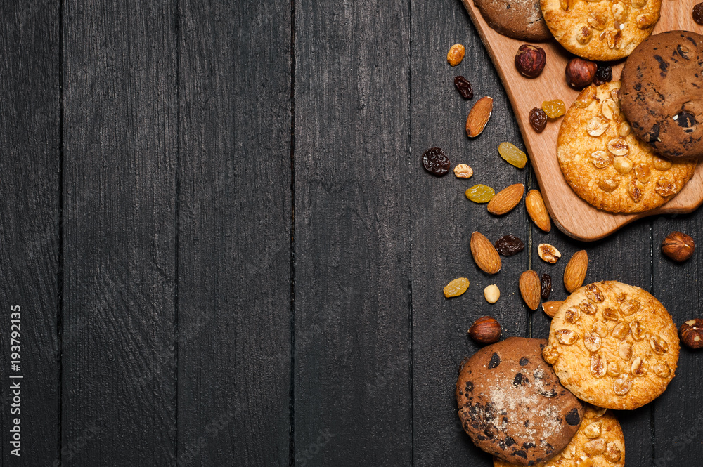 Freshly baked cookies on a wooden table. Lies on a wooden reach, around different nuts, almonds and raisins. Freshly baked cookies on a wooden table. Lies on a wooden reach, around different nuts, almonds and raisins.
