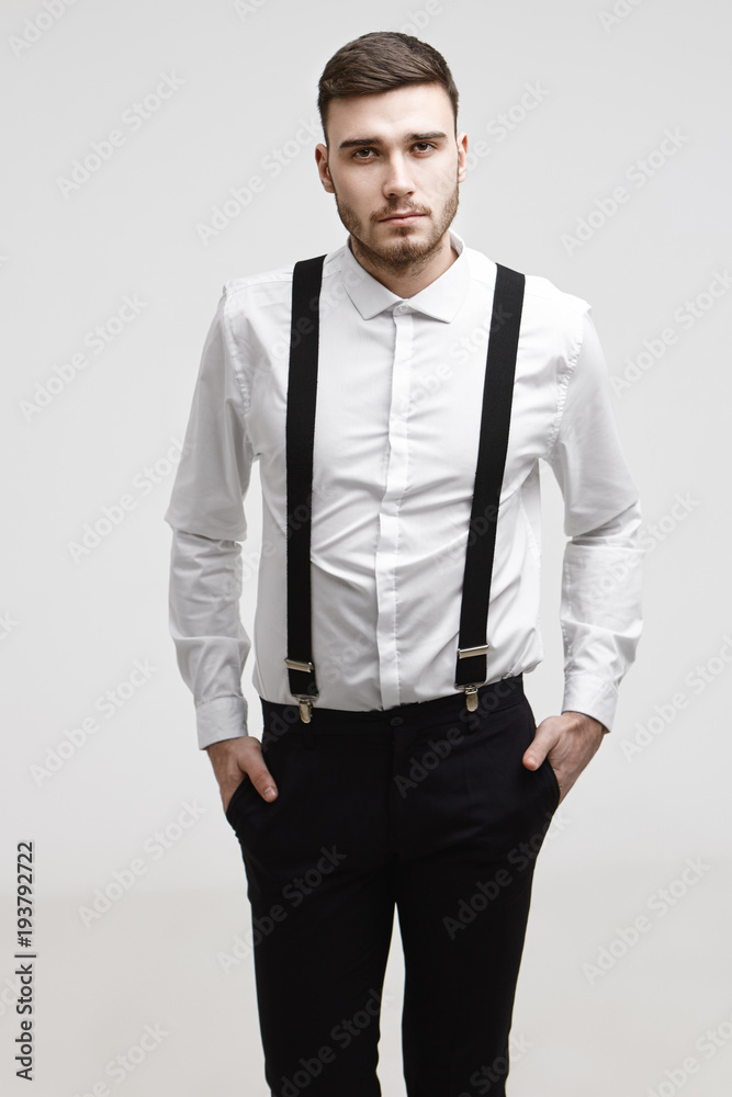 People, business, job, career, style and fashion concept. Attractive confident young European male entrepreneur posing in studio dressed in elegant stylish formal suit, holding hands in pockets People, business, job, career, style and fashion concept. Attractive confident young European male entrepreneur posing in studio dressed in elegant stylish formal suit, holding hands in pockets