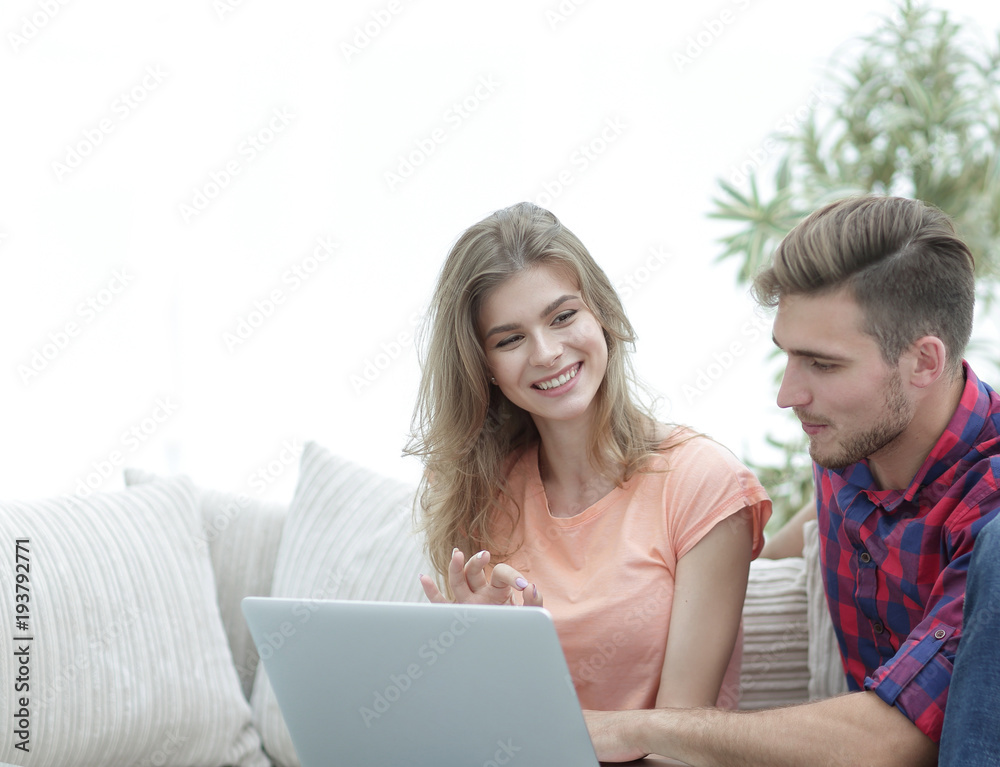 young couple is using a laptop and smiling while sitting on sofa at home