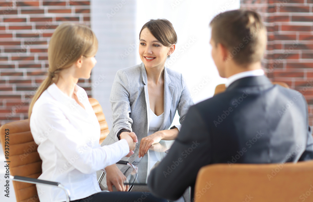 handshake of a Manager, and a client sitting behind a Desk handshake of a Manager, and a client sitting behind a Desk