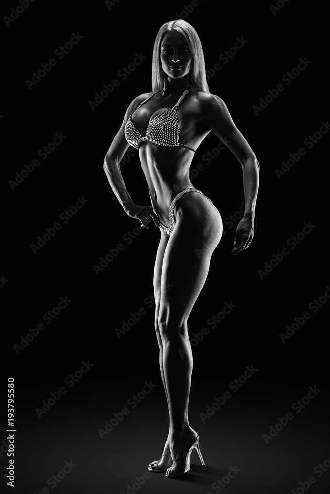 Black and white dramatic photo Fitness bikini model competition championship Female athlete bodybuilder posing on stage Perfect trained body shape legs arms chest Strong muscular sports Clipping path