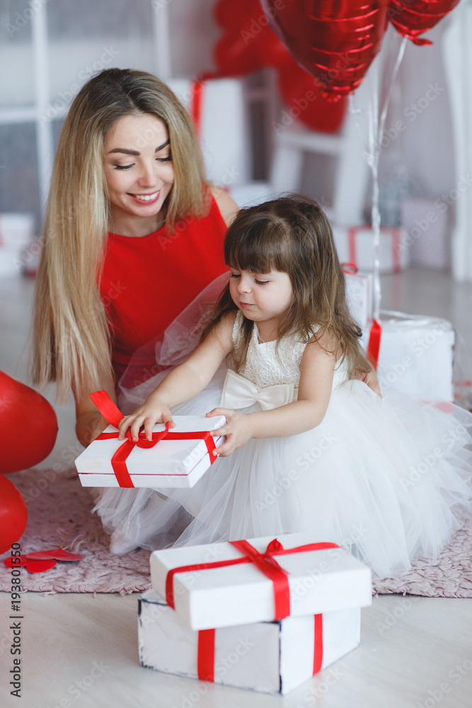 Young beautiful mother and her little daughter,dressed in a beautiful,festive and elegant dress,prepare gifts and red balloons in form of heart for beautiful winter holiday-Valentine's day.
