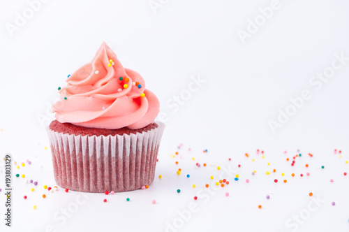 Cupcake red velvet with blue and pink whipped cream decorated with colorful sprinkles on white background.
