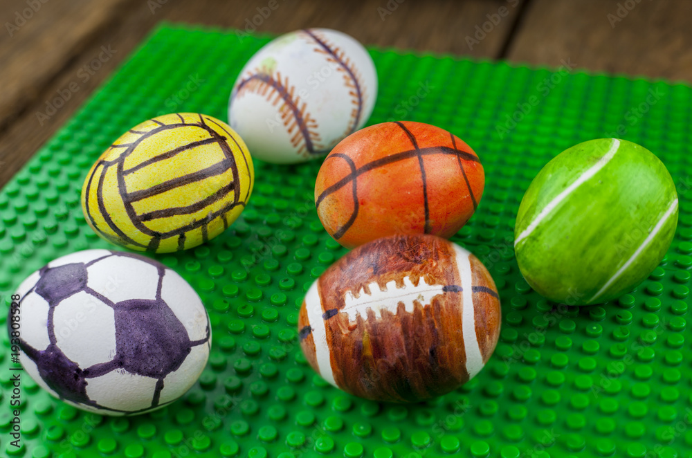 Chicken egg with a pattern under sports balls, on the green background.