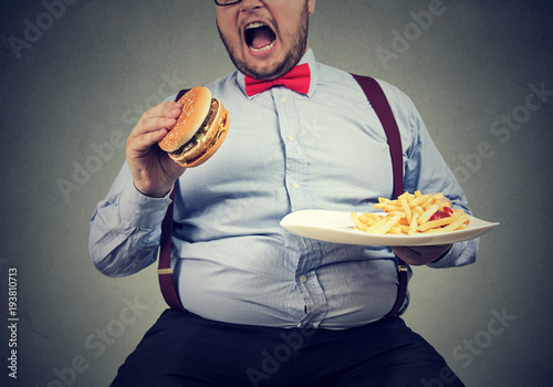 big man in formal clothes sitting and consuming plate with fast food