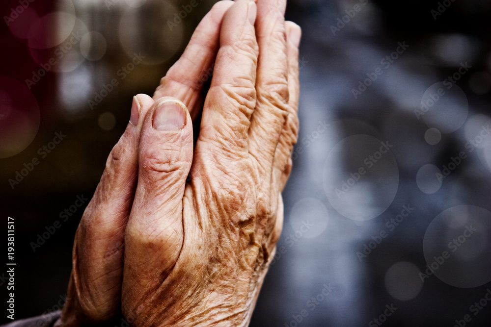 Fototapeta premium Hands of the old grandmother in prayer on a light background