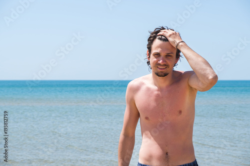 Handsome man posing on beach, portrait. Hand in hair.