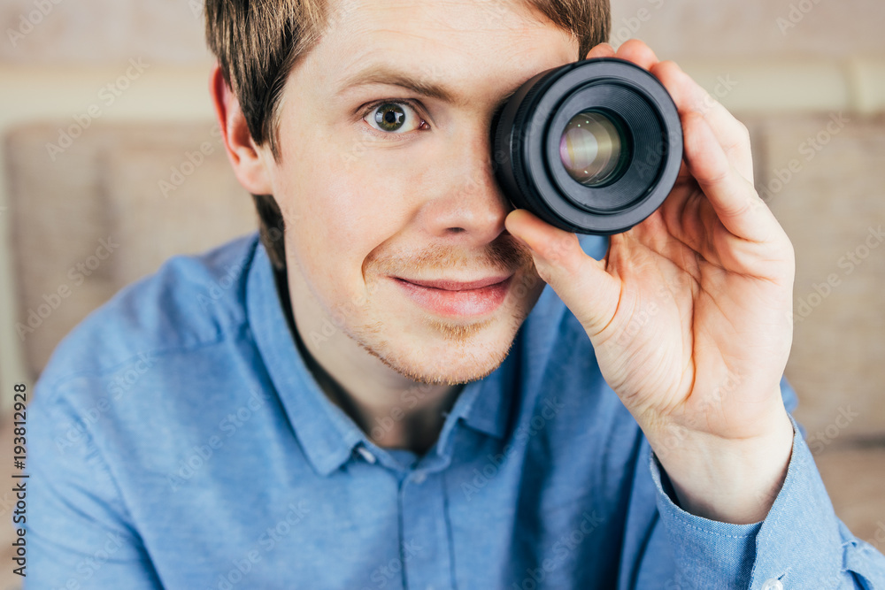 Young male photographer holds camera lens in his eye. Close-up Young male photographer holds camera lens in his eye. Close-up