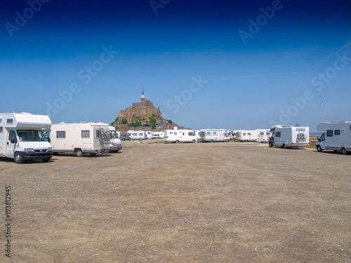 Parking area for camper vans with Mont Saint Michel in the background on a sunny day with a clear blue sky